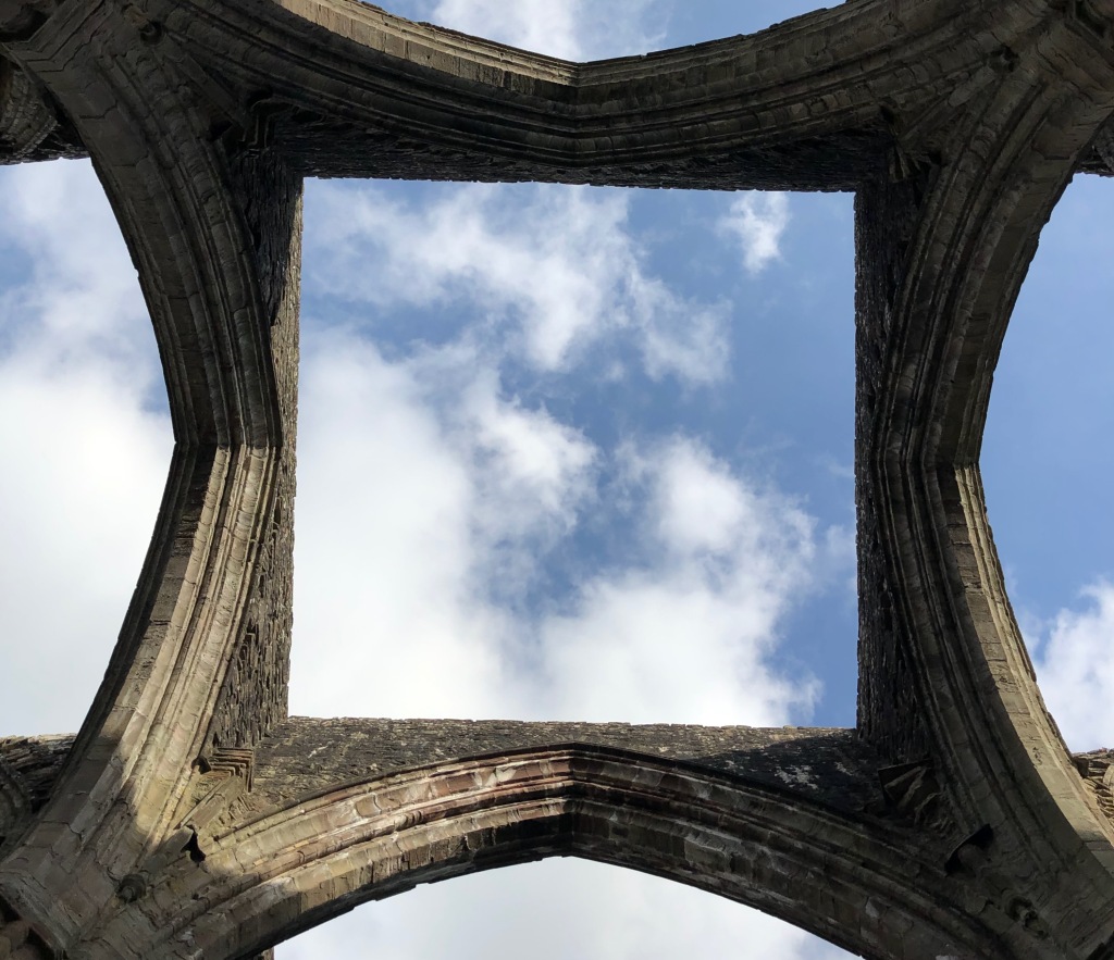 Tintern Abby view through destroyed roof to blue sky and puffy clouds.